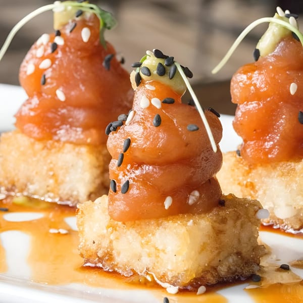 Three Craft House tuna tartare appetizers on crispy rice, garnished with sesame seeds and microgreens.