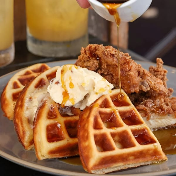 Maple syrup being poured over Craft House's chicken and waffles with butter and orange juice.