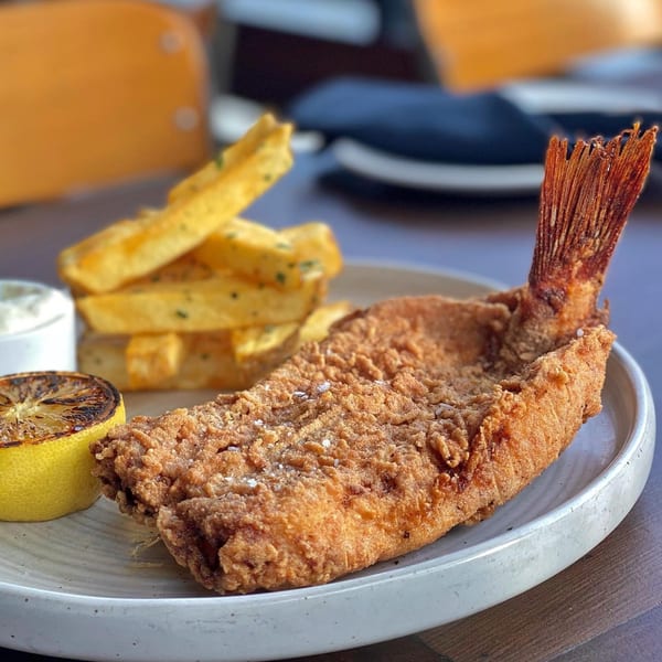 Crispy fried whole fish with tail, served with thick-cut fries, grilled lemon, and dipping sauce.
