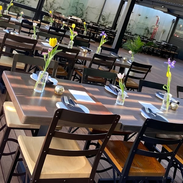 Outdoor dining area with wooden tables, chairs, and small vases of flowers on each table.