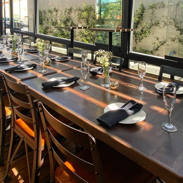 Long dining table set with plates, black napkins, champagne flutes, and small flower arrangements.