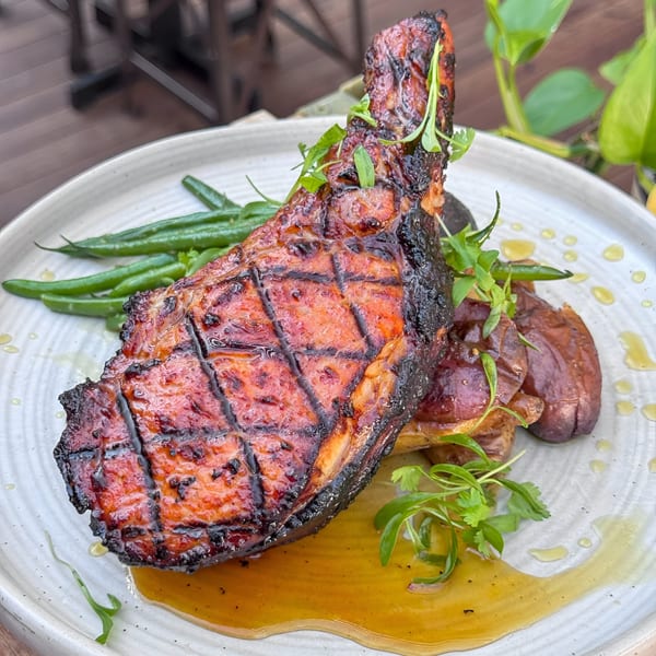 Grilled pork chop with green beans, roasted potatoes, and a golden sauce on a white plate.